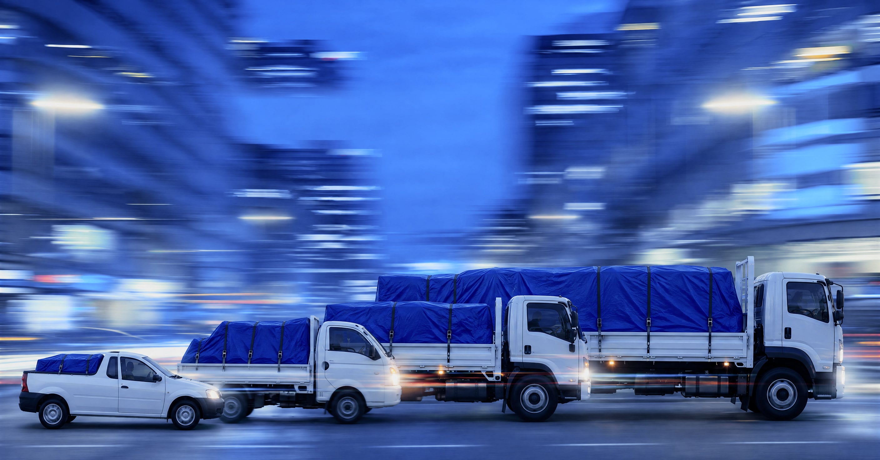 Bakkies and trucks with blue-covered loads on a city road at dusk