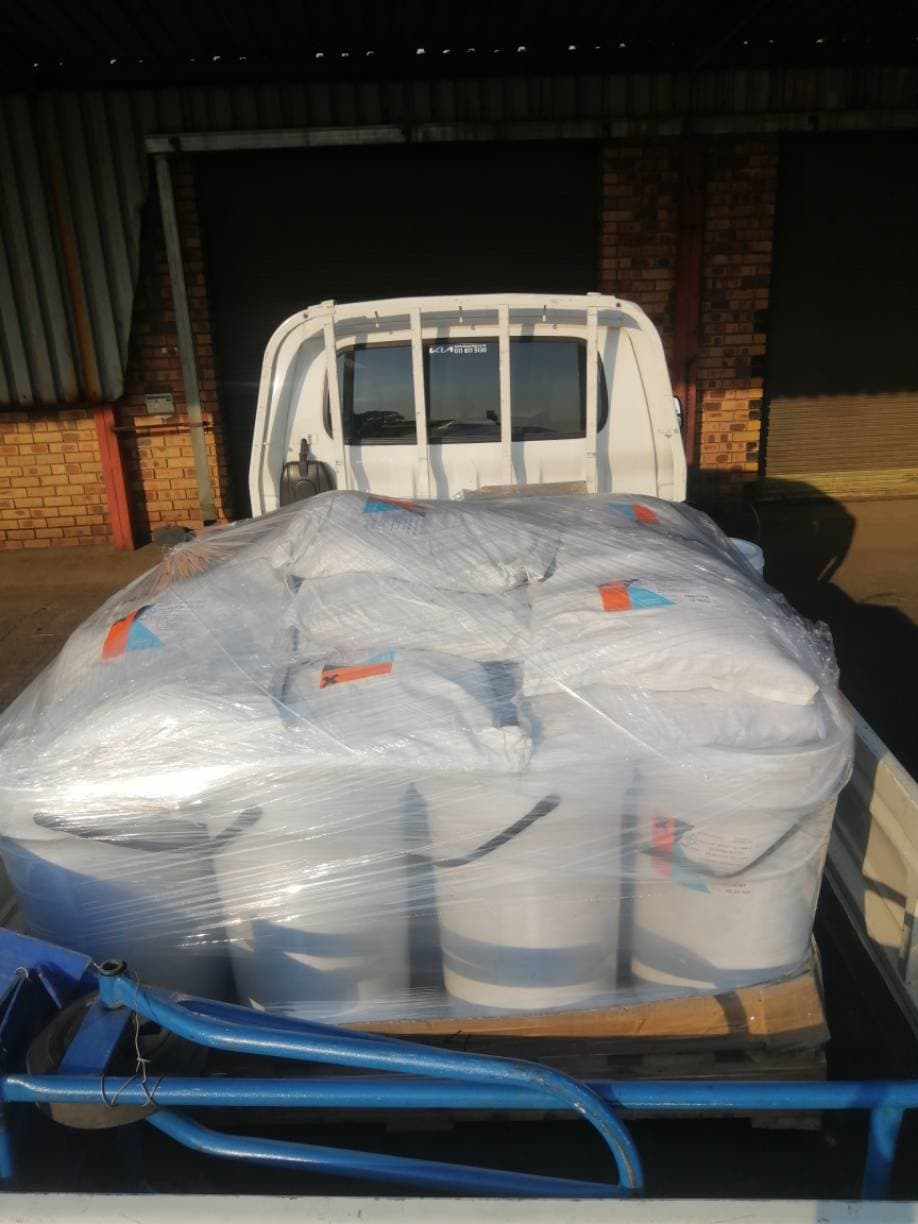 A shrink-wrapped pallet of bagged goods strapped on a bakkie at a warehouse loading bay